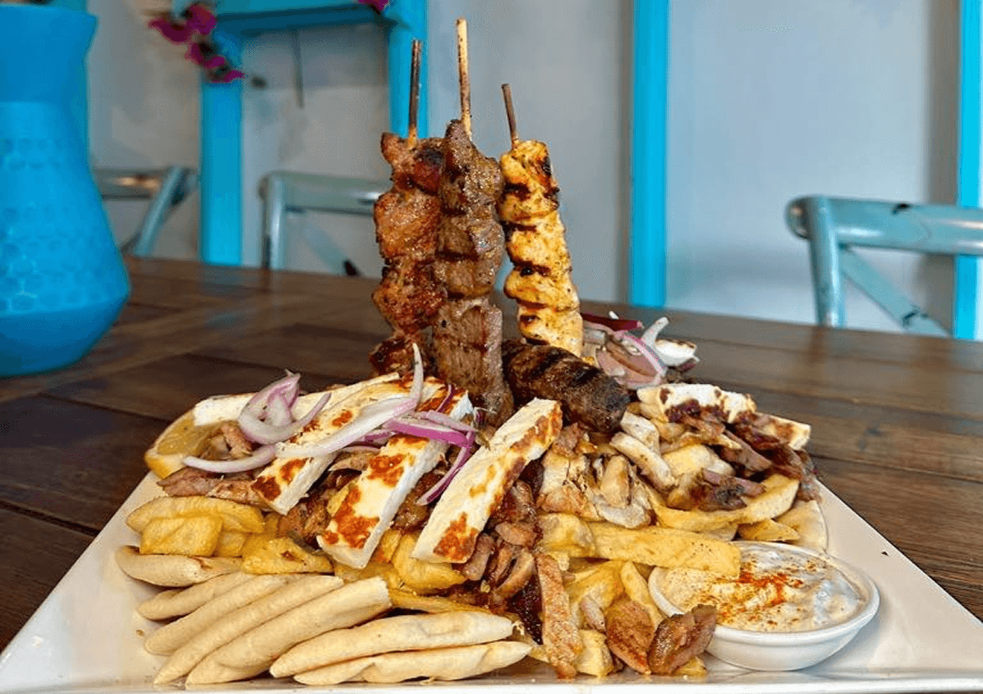 A large shared Greek platter of grilled meats, dips and pita for a group table